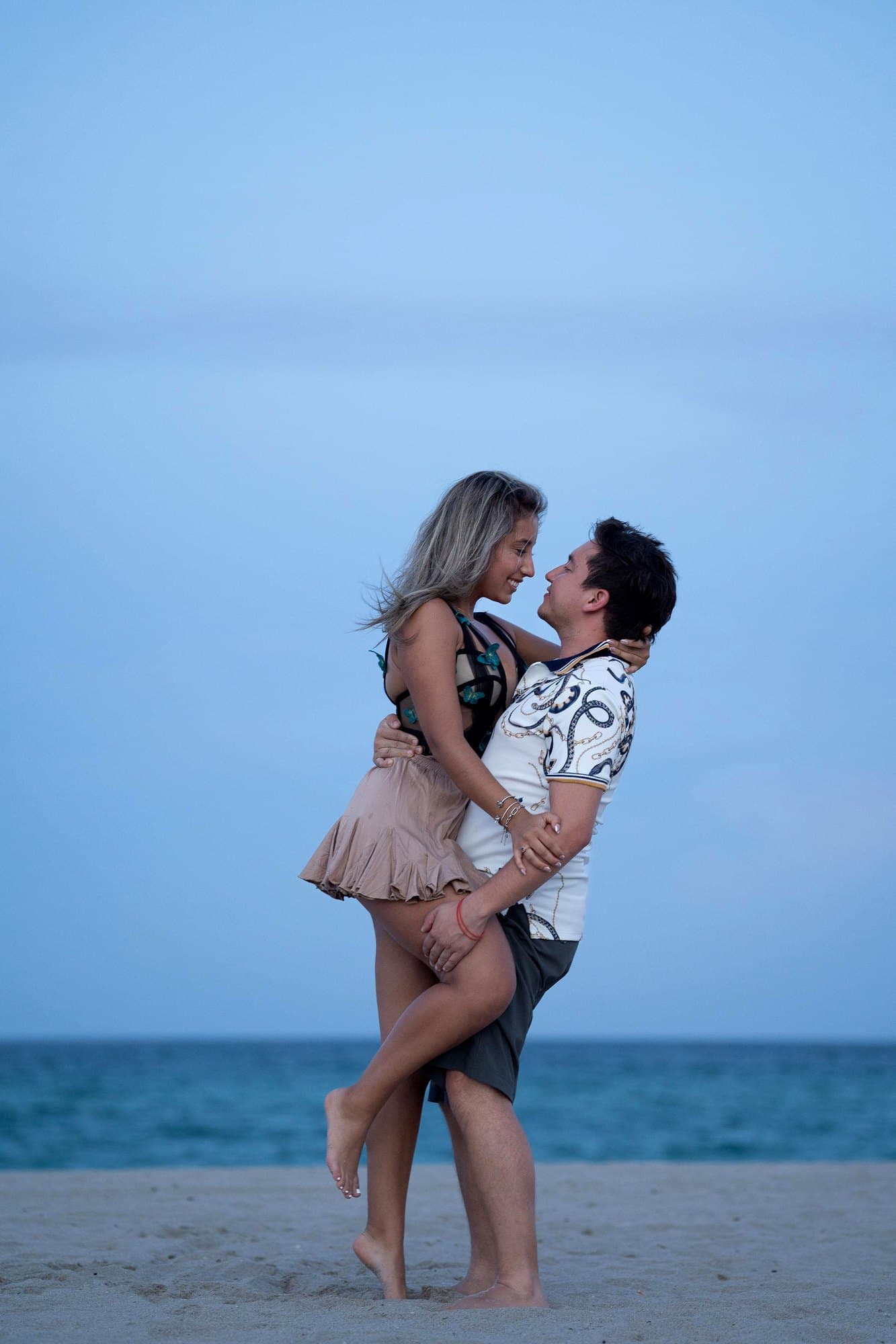 La pareja abrazada en la playa, con el mar detrás