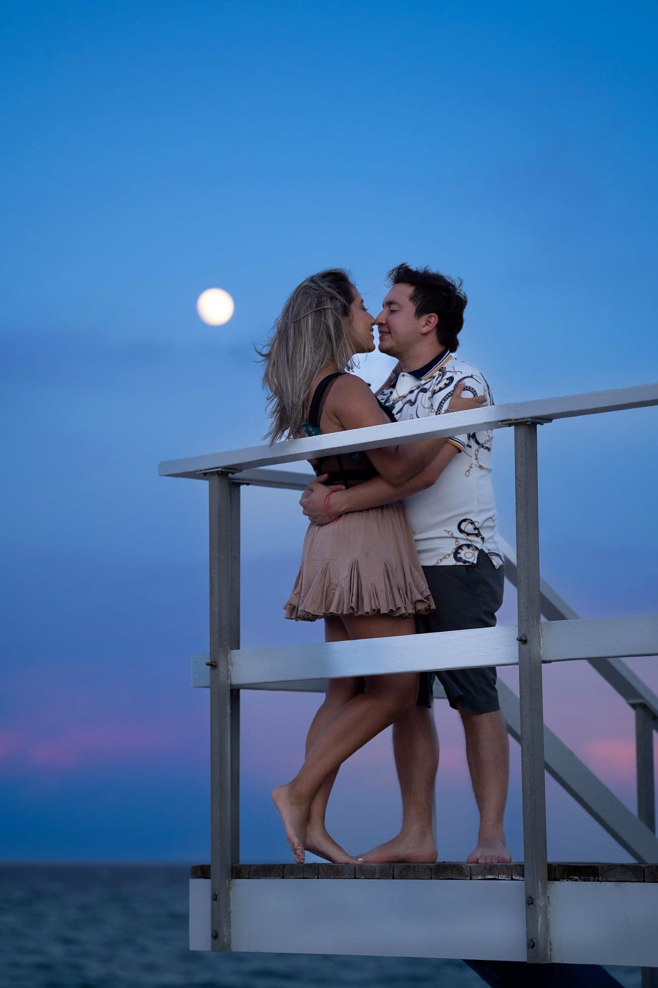 La pareja frente al mar con la luna llena sobre el horizonte